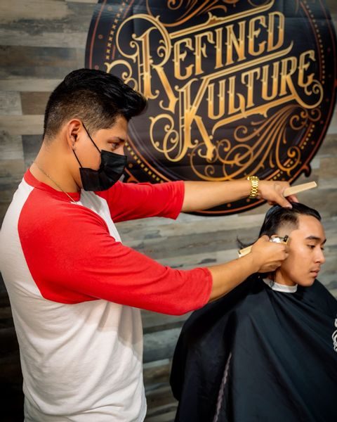 A Refined Kulture barber at work in front of the studio's gold logo wall